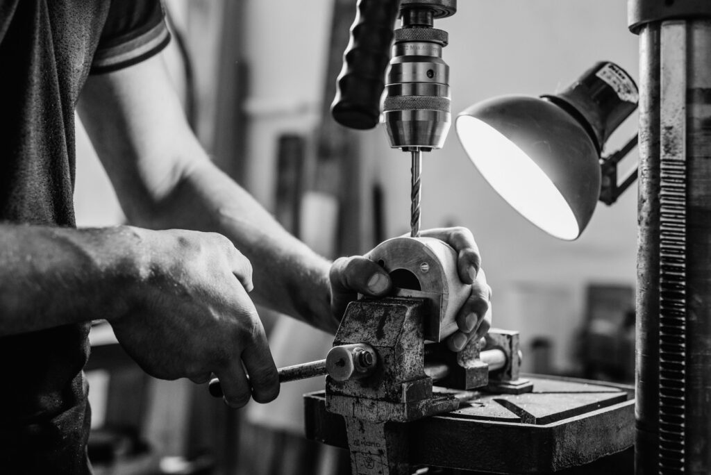 pexels-photo-7190982-7190982 Black and white close-up of a worker using a drill press in a workshop.